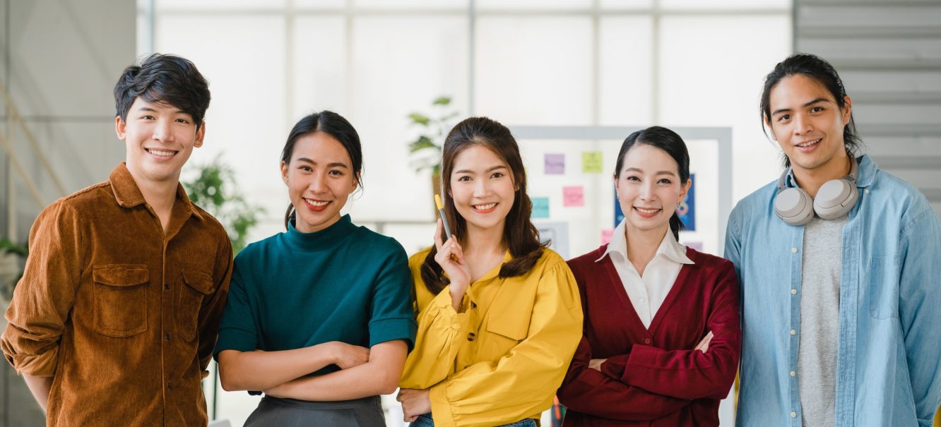 Group of Asia young creative people in smart casual wear smiling and arms crossed in creative office workplace. Diverse Asian male and female stand together at startup. Coworker teamwork concept.